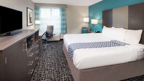 Hotelkamer met een bed, een bureau met een flatscreen televisie, een stoel, een lamp en een raam met gordijnen.