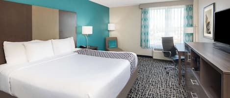 A hotel room with a large bed, a desk, a chair, and a television.
