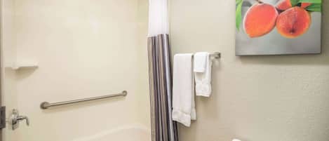 Un baño con una bañera blanca, ducha con puerta de cristal, barandilla y un inodoro. Hay un cuadro de frutas en la pared.