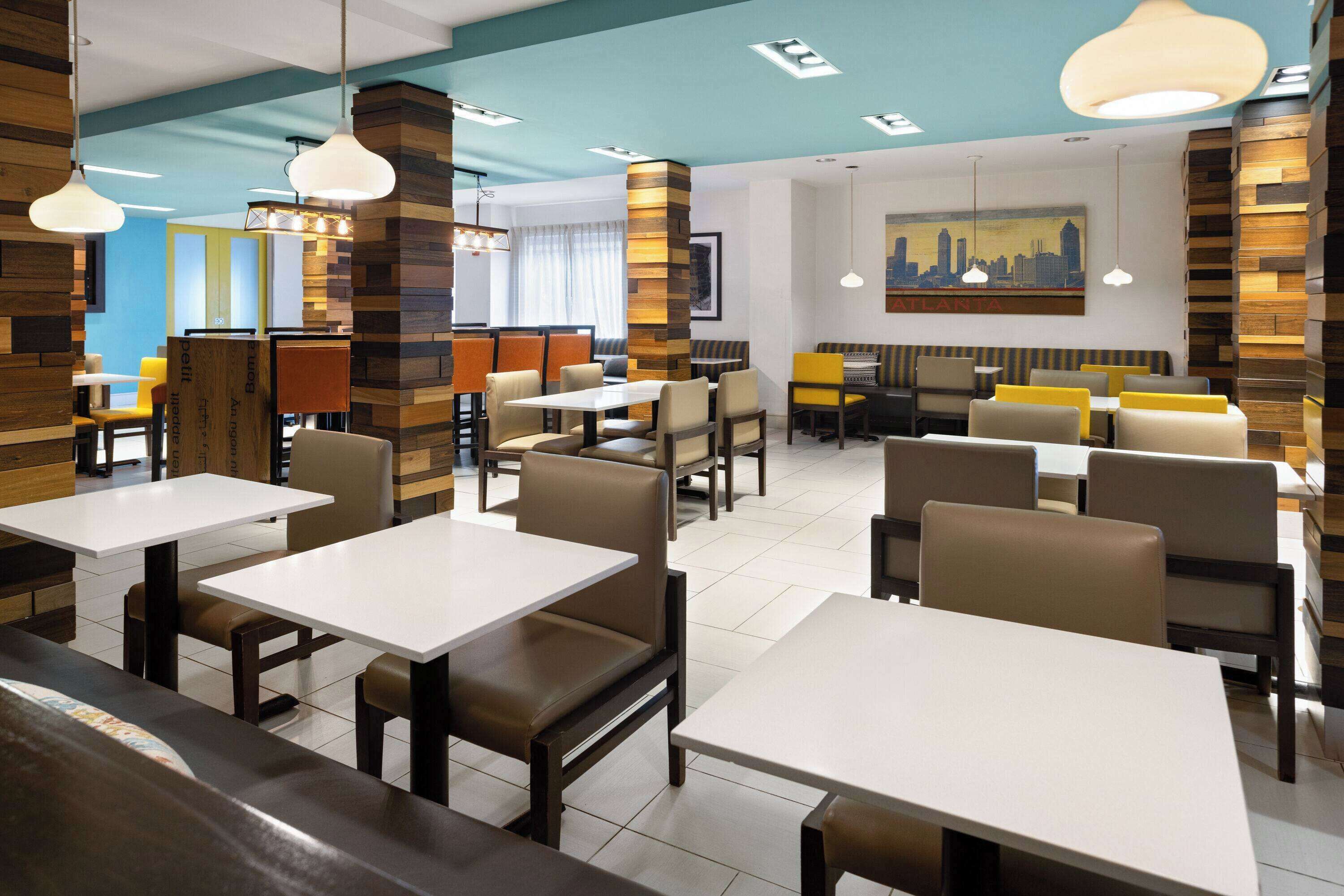 A modern restaurant interior with multiple dining tables and booths, wooden accents on the walls, and a cityscape painting on the wall.