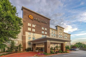 Un hôtel La Quinta au design moderne, avec un logo solaire bien visible, plusieurs étages et un espace d’entrée abrité.