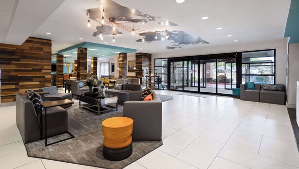 Een ruime lobby met modern meubilair, een groot zitgedeelte en uitzicht door de glazen deuren.