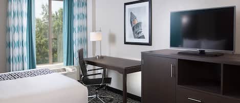 A hotel room with two beds, a desk, a chair, a television, and a framed picture on the wall.