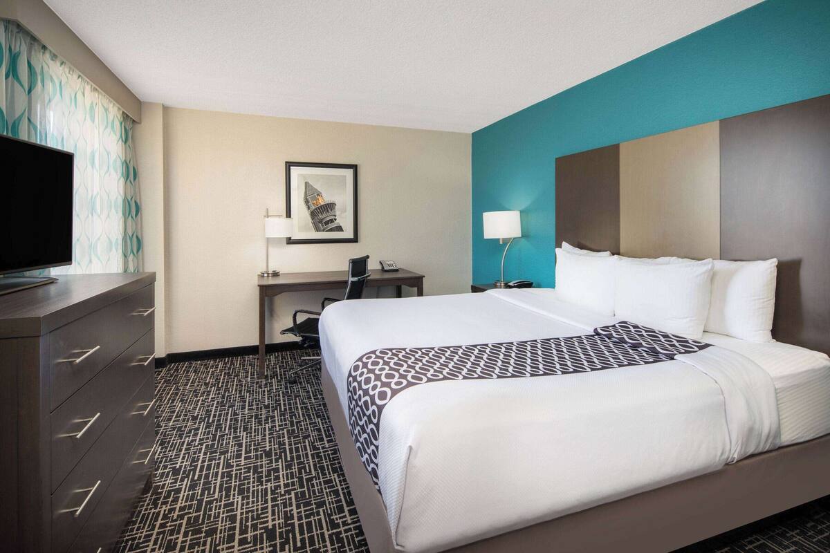 Une chambre d’hôtel avec un lit, un bureau, une télévision et une moquette à motifs.