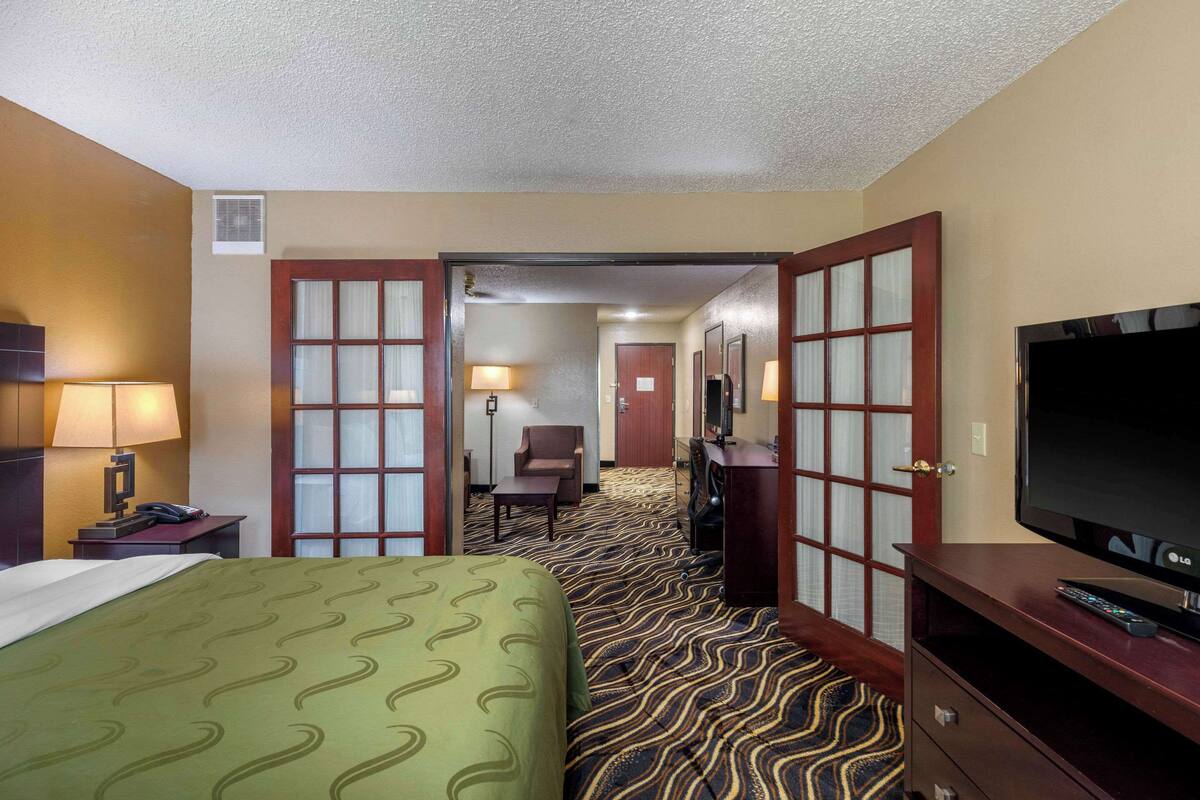 A hotel room with a bed, a TV, a desk with a lamp, and a chair.