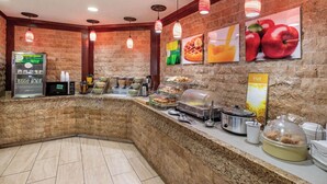 Ein Bereich mit Frühstücksbuffet, einer Selbstbedienungsstation, einer Mikrowelle und verschiedenen Speisen.