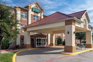 A hotel with a covered entrance, a sign reading "Quality Suites," and a brick facade.