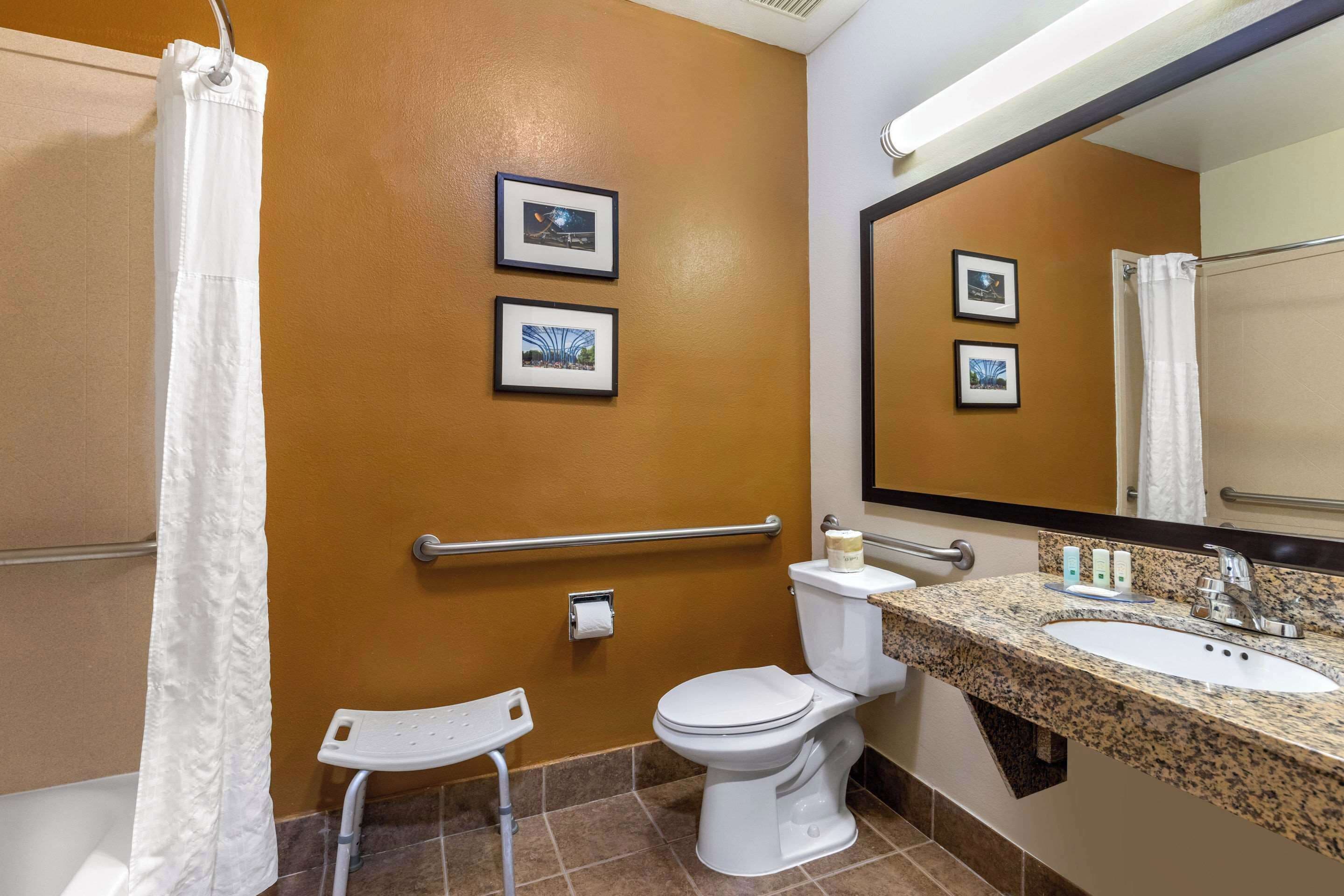 Un baño con inodoro blanco, un lavamanos con encimera de granito, un espejo y dos cuadros en la pared.