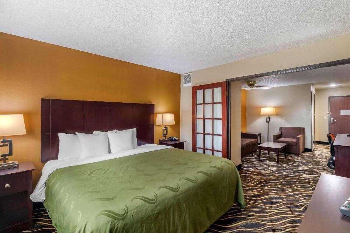 Une chambre d’hôtel comprenant un lit, des tables de chevet, un bureau, une chaise et une porte donnant sur une autre pièce.