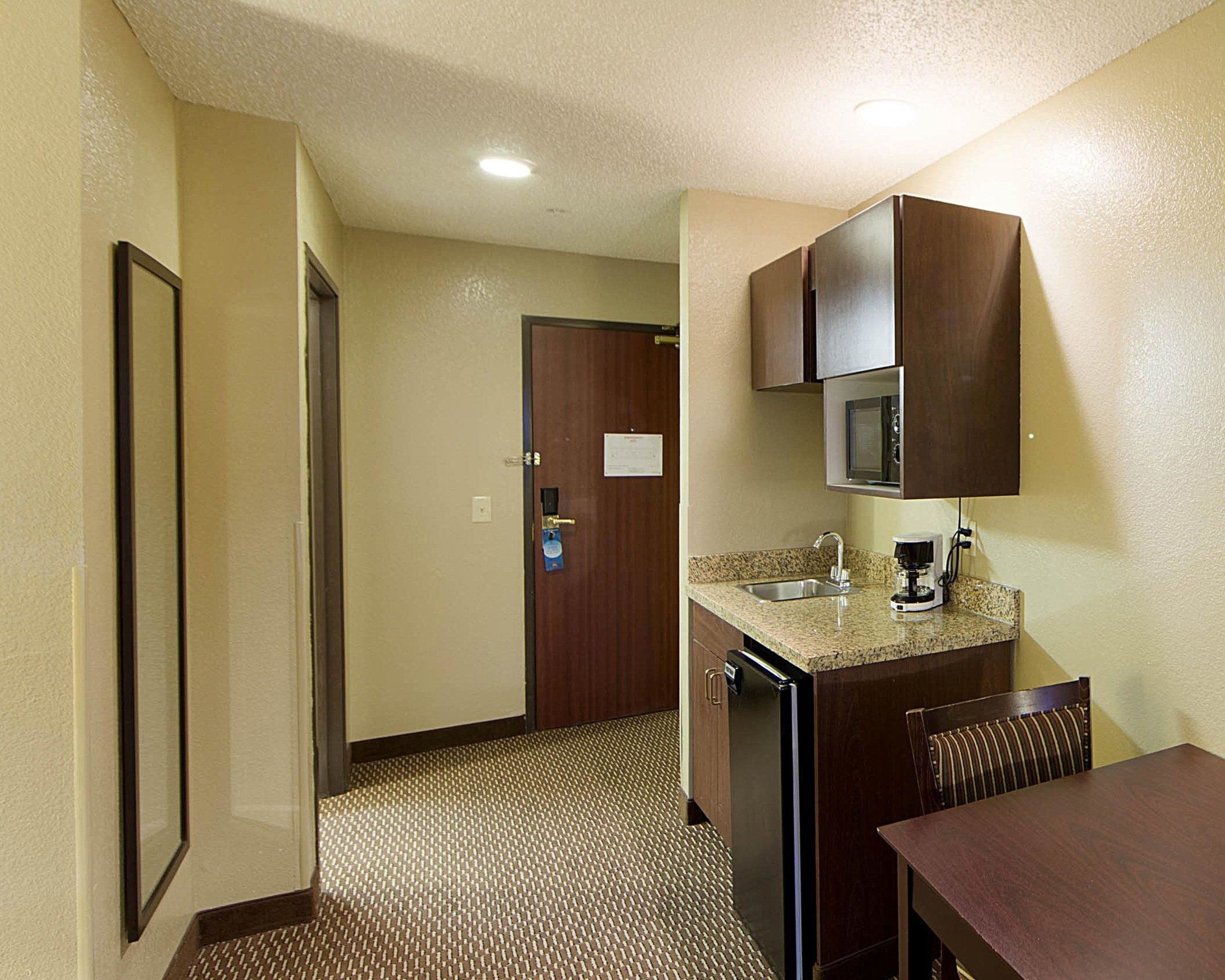 Habitación de hotel compacta con kitchenette, microondas, cafetera y refrigerador pequeño.