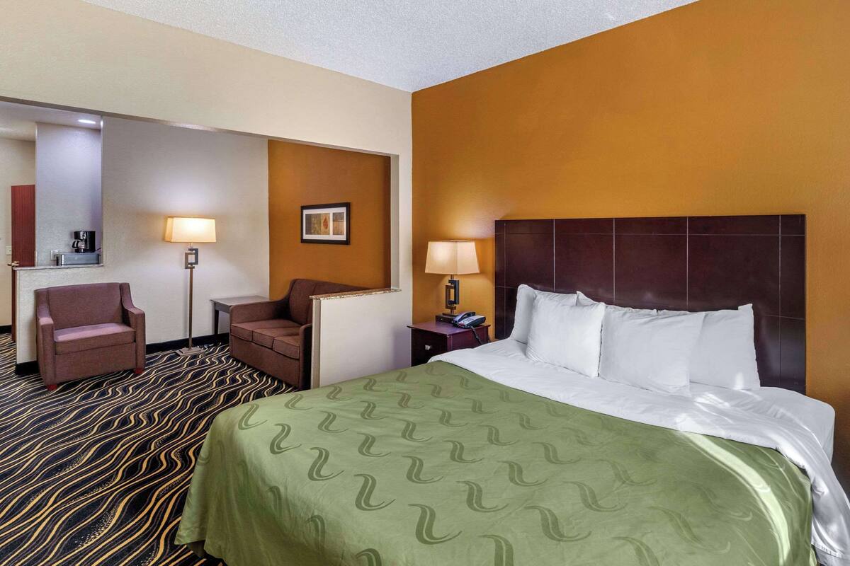 A hotel room with a bed, two chairs, a desk, a lamp, and a framed picture on the wall.