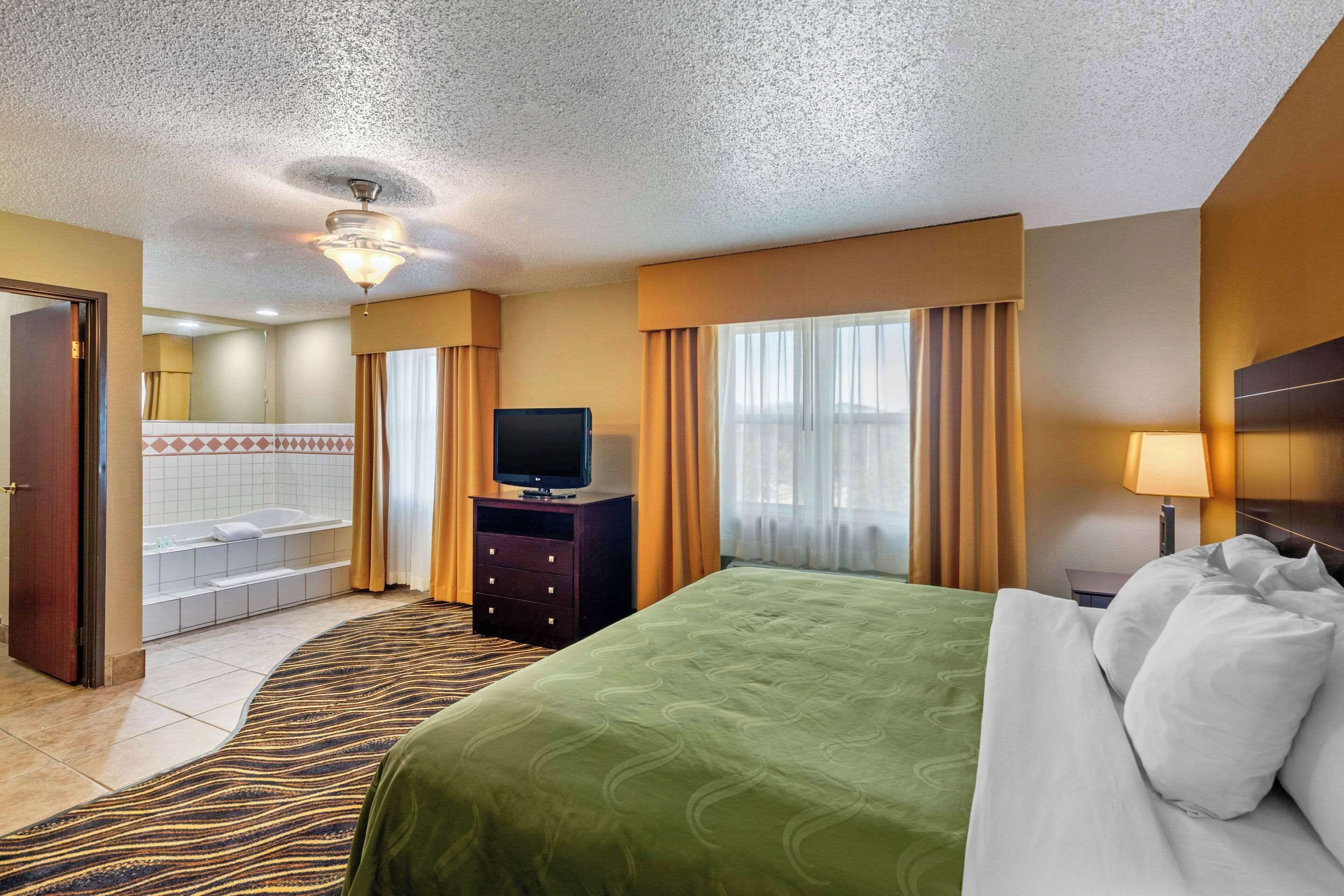 A hotel room with a bed, a television, a dresser, a bathroom with a bathtub, and a window with curtains.