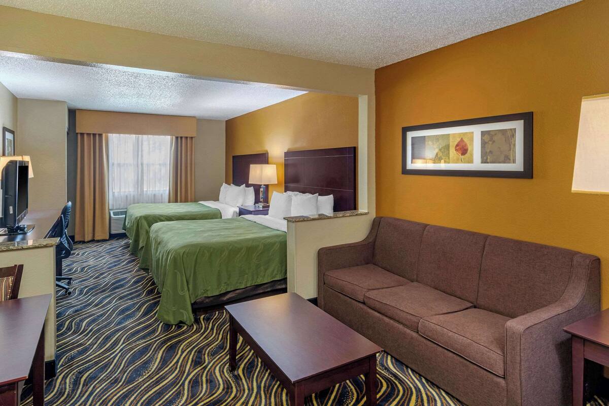 A hotel room with two beds, a sofa, a desk, and a television.