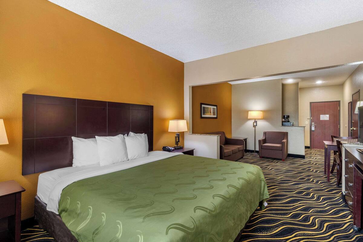 A hotel room with a large bed, a desk, a chair, and a small kitchenette.