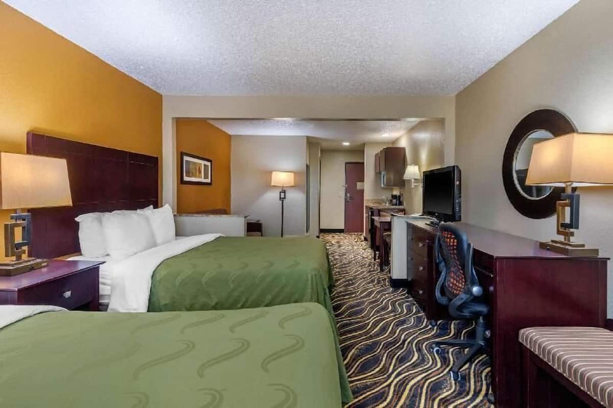 A hotel room with two beds, a desk with a chair, a television, and a mirror.