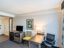 Habitación de hotel con escritorio, una silla, televisor, microondas y un cuadro en la pared.