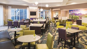 A hotel lobby with multiple seating areas, a television mounted on the wall, and a large window offering a view of the outdoors. - La Quinta Inn & Suites by Wyndham Phoenix Chandler (Phoenix)
