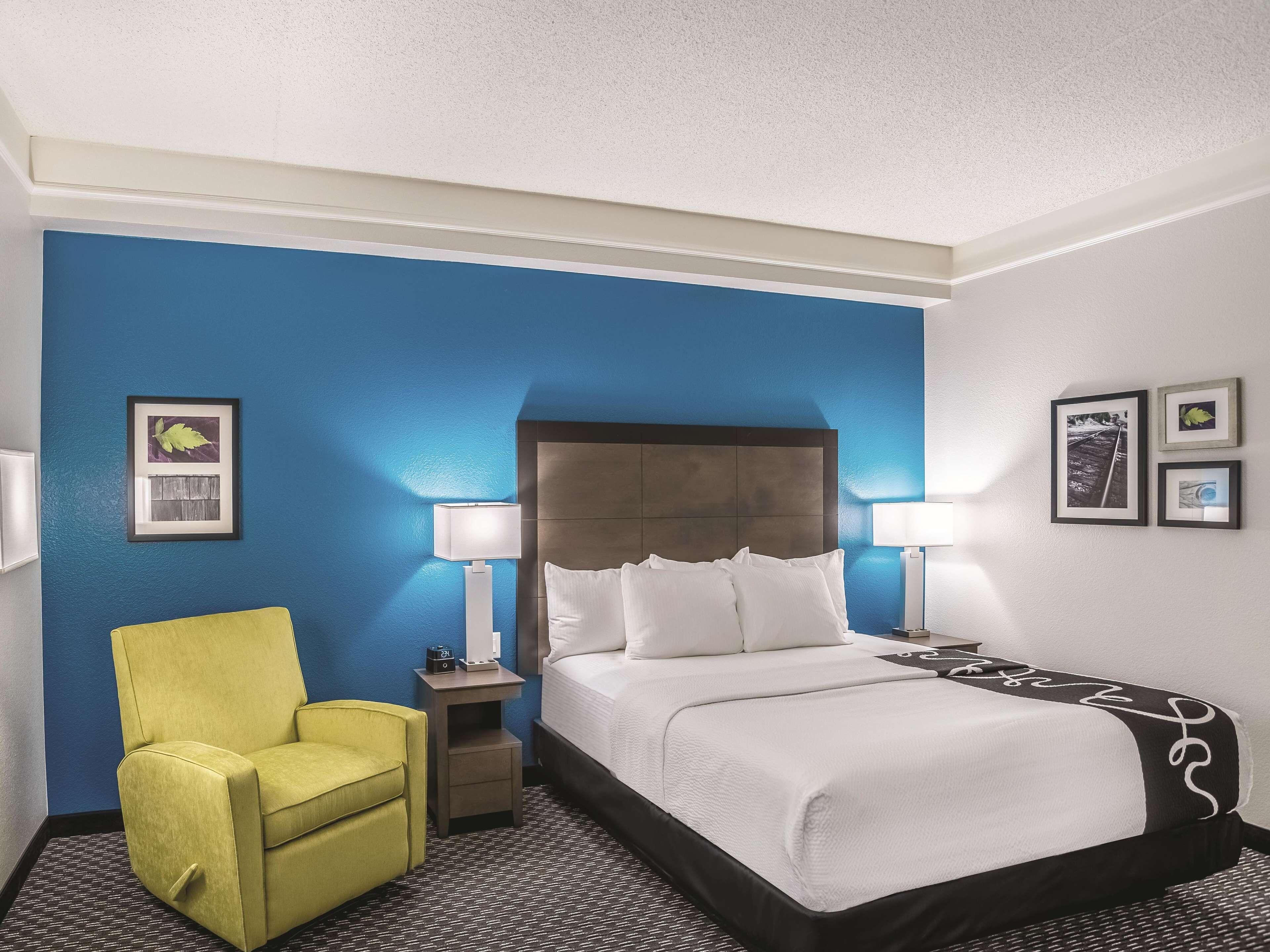 A hotel room with a large bed, a yellow armchair, and a nightstand with a lamp.
