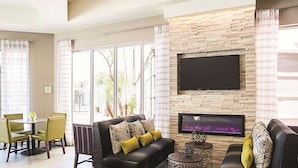 A modern living room with a fireplace, a sofa, a coffee table, and a TV mounted on the wall. - La Quinta Inn & Suites by Wyndham Phoenix Chandler (Phoenix)