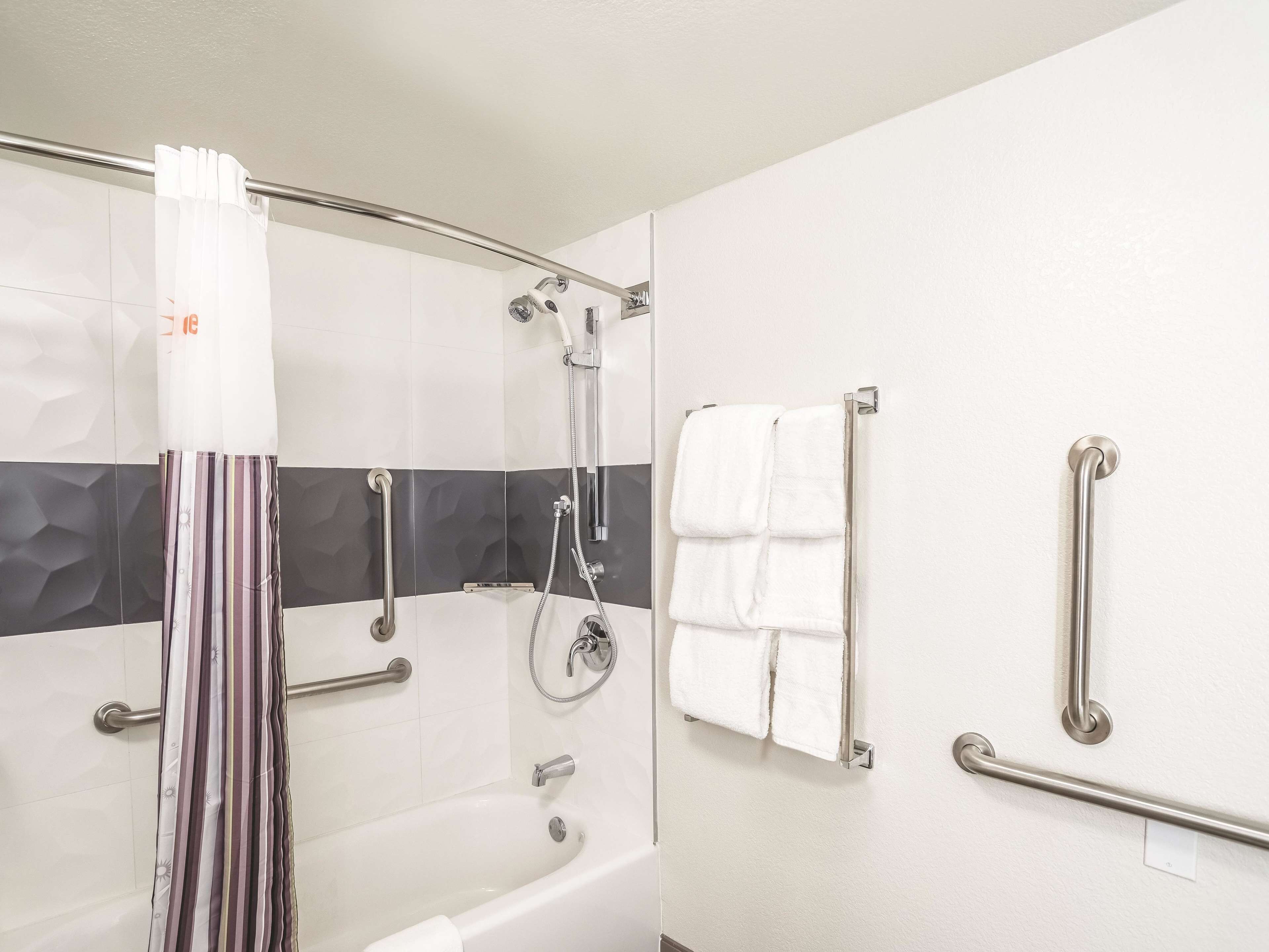A modern bathroom with a bathtub, a shower, and a toilet. It includes grab bars and a towel rack.