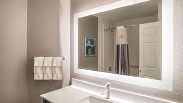 Un baño con un espejo grande, un lavabo y un perchero con toallas.