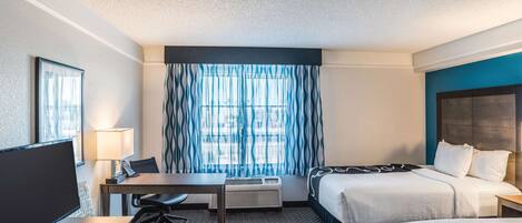 Une chambre d’hôtel avec un lit, un bureau et une chaise, une télévision et une fenêtre avec des rideaux.