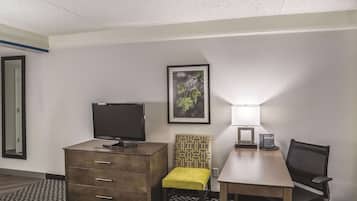 A hotel room with a desk, chair, television, and a framed picture on the wall.