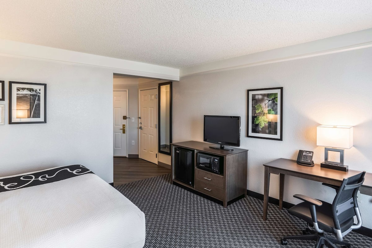 A hotel room with a bed, a desk with a computer, a TV, a lamp, and framed pictures on the wall.