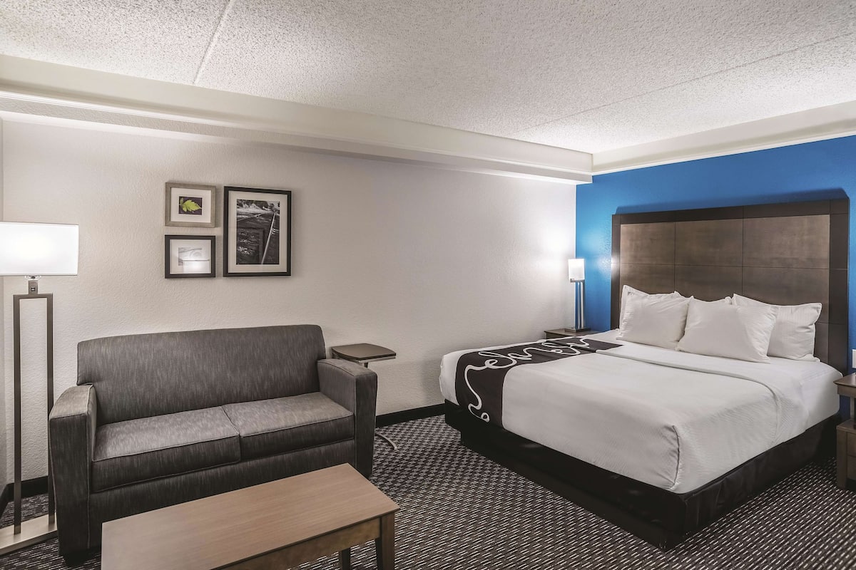 A hotel room with a bed, a sofa, a small table, and two bedside lamps.
