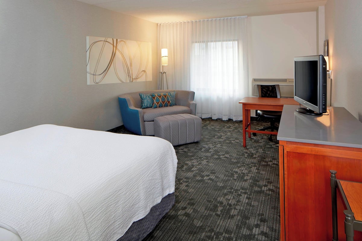 A hotel room with a large bed, a sofa, a desk with a computer, and a television.
