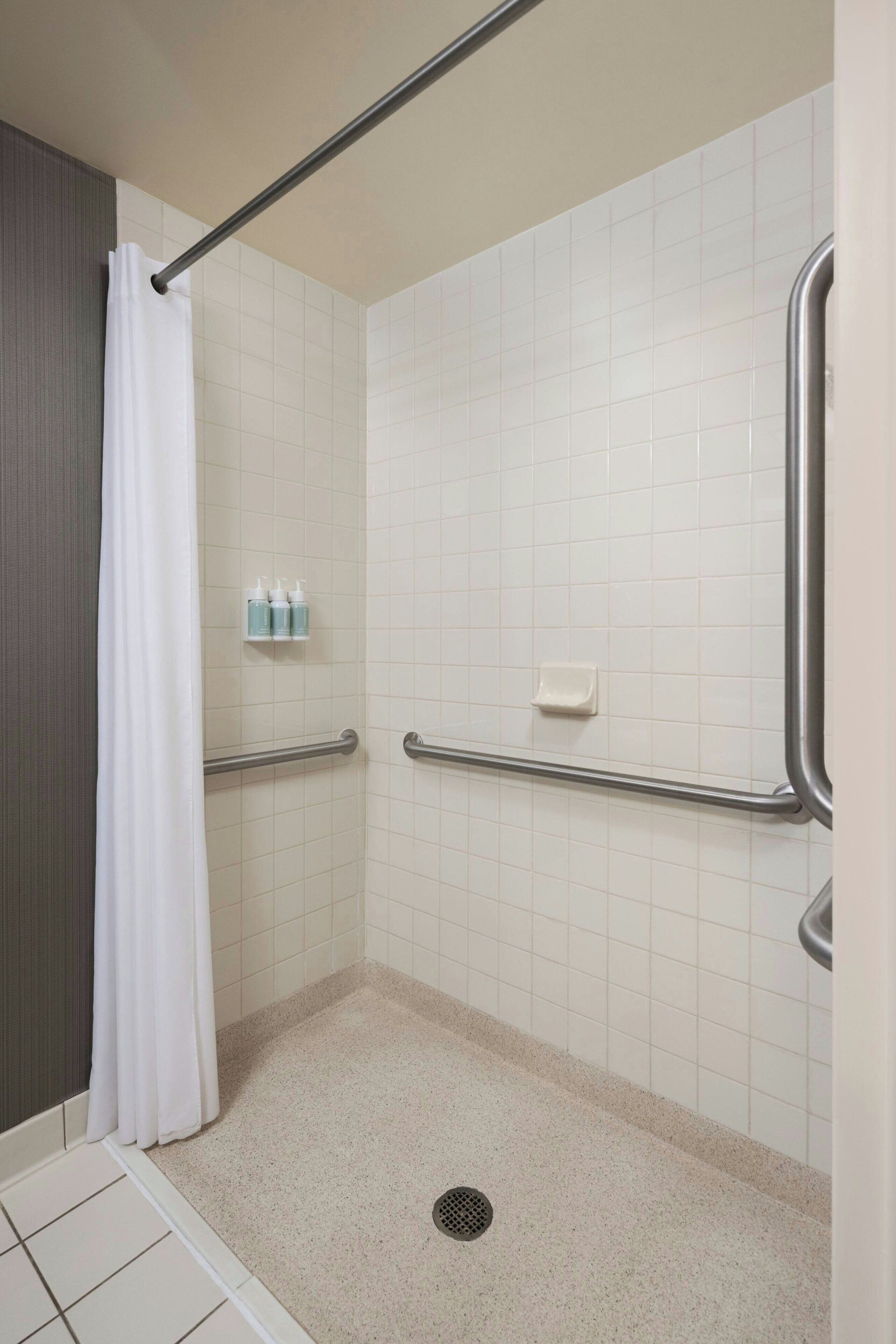 A handicap-accessible shower with a white curtain, grab bars, and a tiled floor.