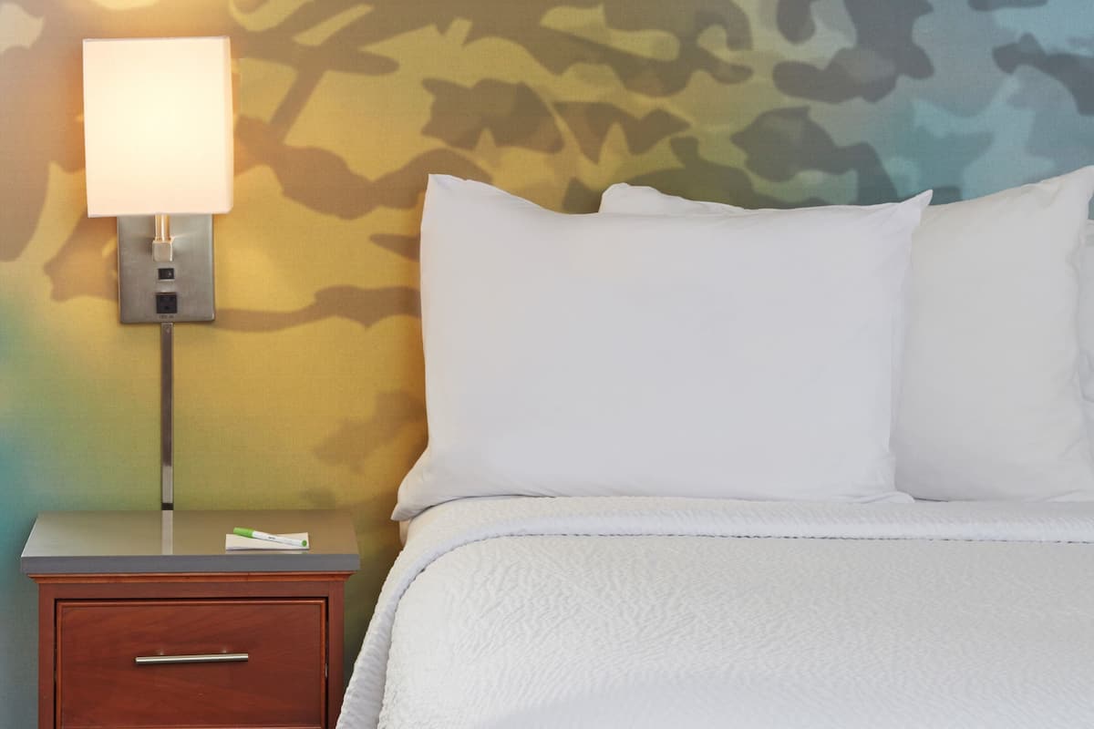 A neatly made bed with white bedding, a bedside lamp, and a wooden nightstand with a drawer.