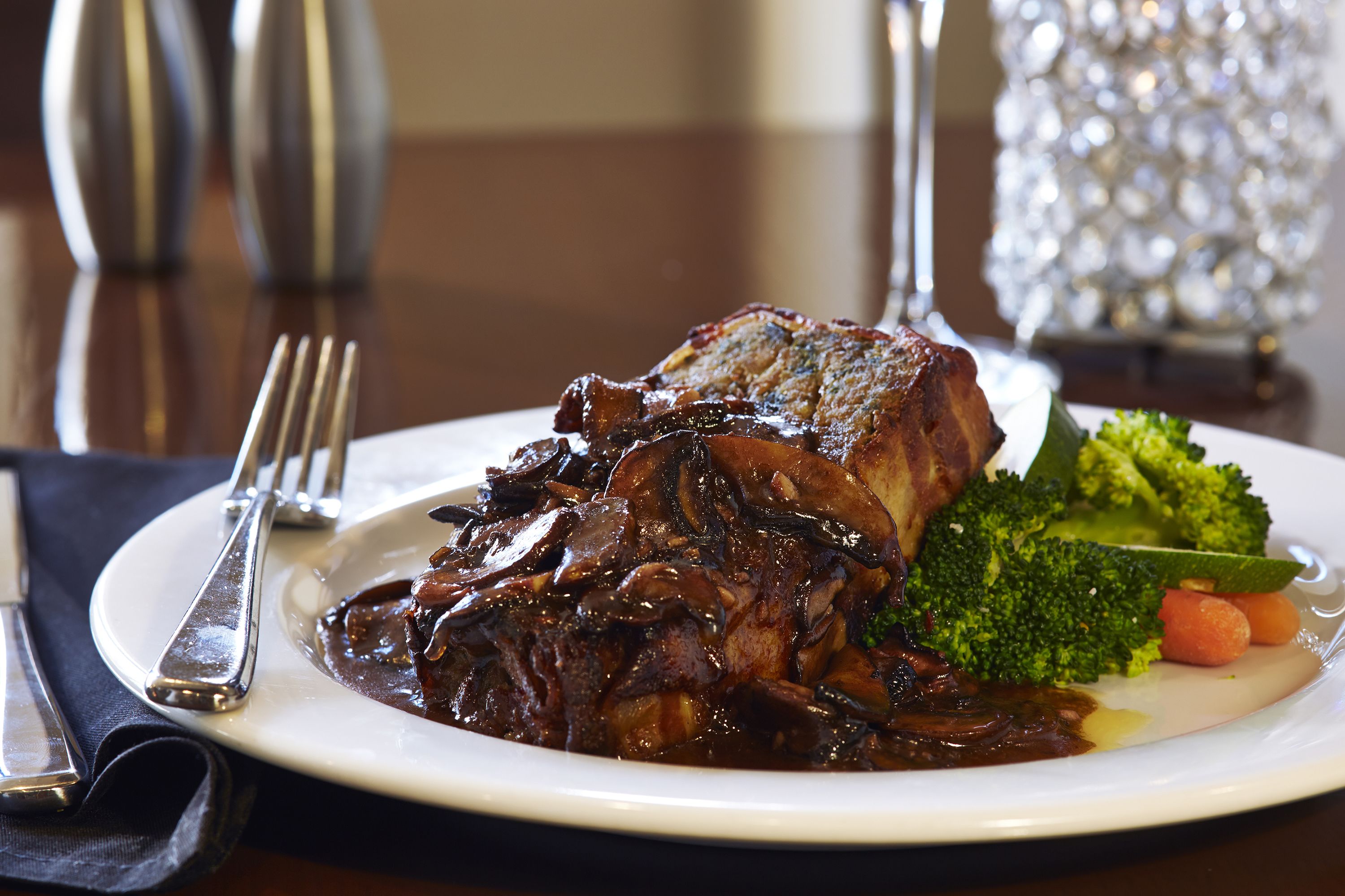 A plate of food with a large piece of meat, vegetables, and a sauce.