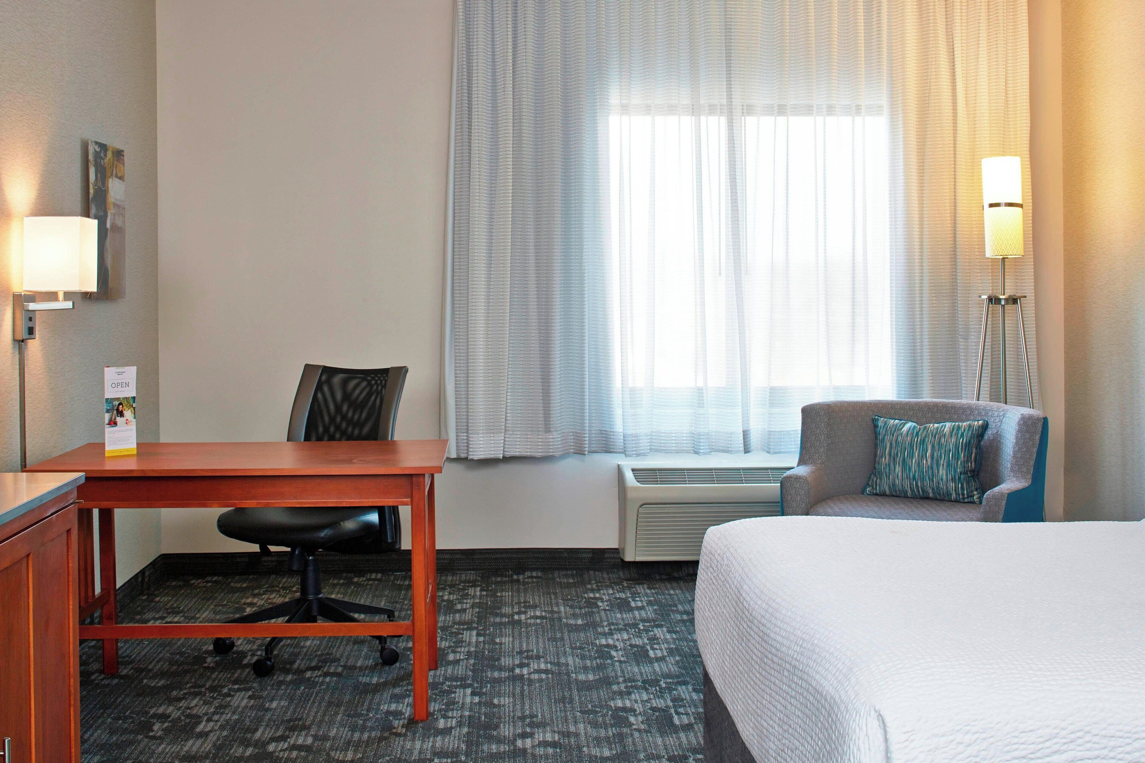 A hotel room with a bed, a desk, a chair, and a window with curtains.