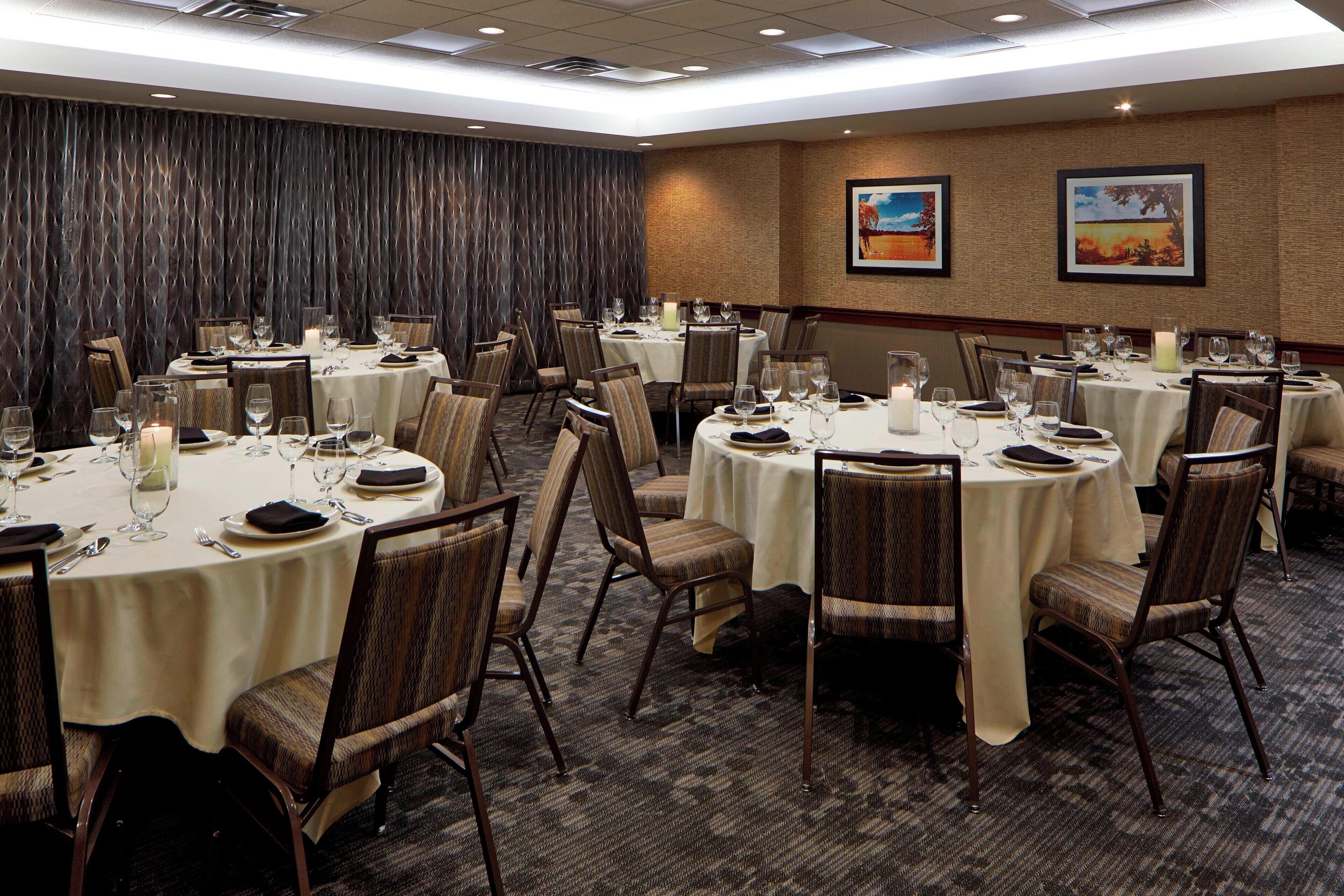 A conference room with multiple round tables, each set with chairs, plates, cutlery, and candles.