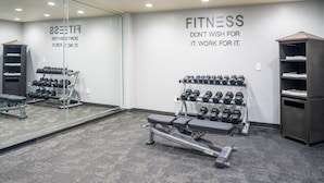 Une salle de sport équipée d’un banc de développé couché, d’haltères et d’un mur recouvert de miroirs sur lequel figurent des messages motivants.