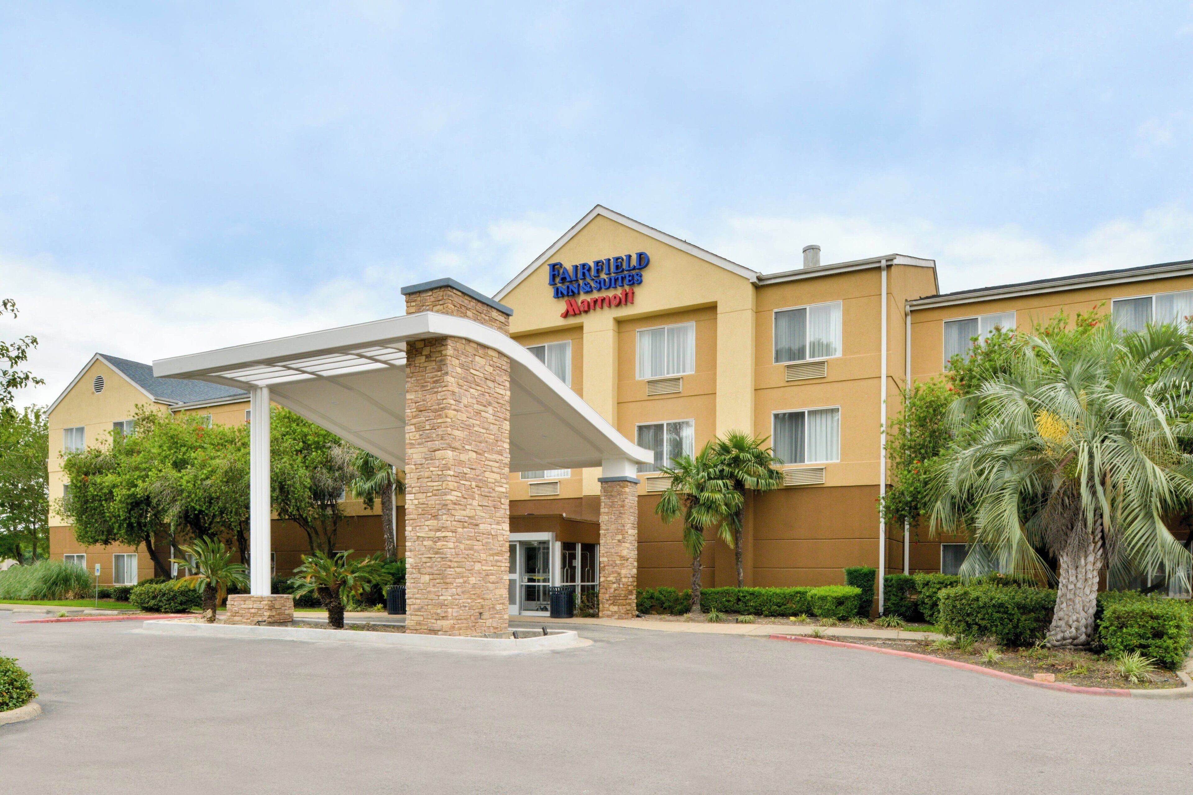 A Fairfield Inn & Suites by Marriott hotel with a covered entrance, palm trees, and a clear sky.