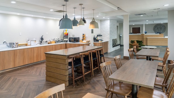 Un restaurant moderne doté d’un bar central, de tables et de chaises en bois, et d’un éclairage suspendu.