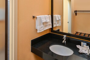 Une salle de bain avec un lavabo noir, un miroir et deux serviettes blanches suspendues à un porte-serviettes.