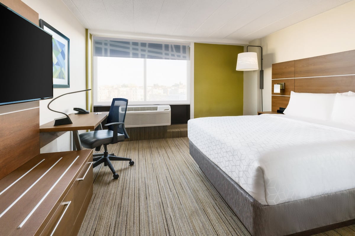 Een hotelkamer met een bed, bureau, stoel en een groot raam.
