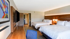 A hotel room with two beds, a flat-screen TV, a wooden headboard, and a colorful abstract painting on the wall.