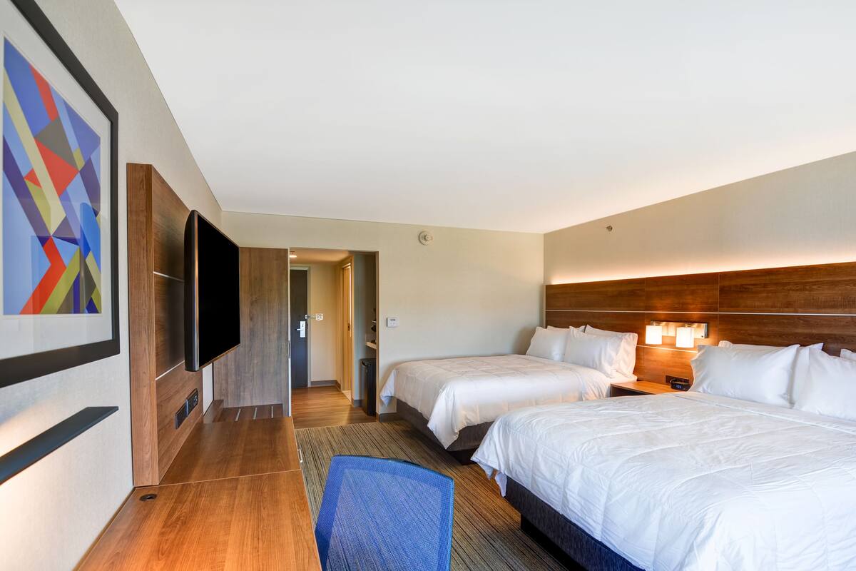 Een hotelkamer met twee bedden, een flatscreen televisie, een houten hoofdeinde en een kleurrijk abstract schilderij aan de muur.