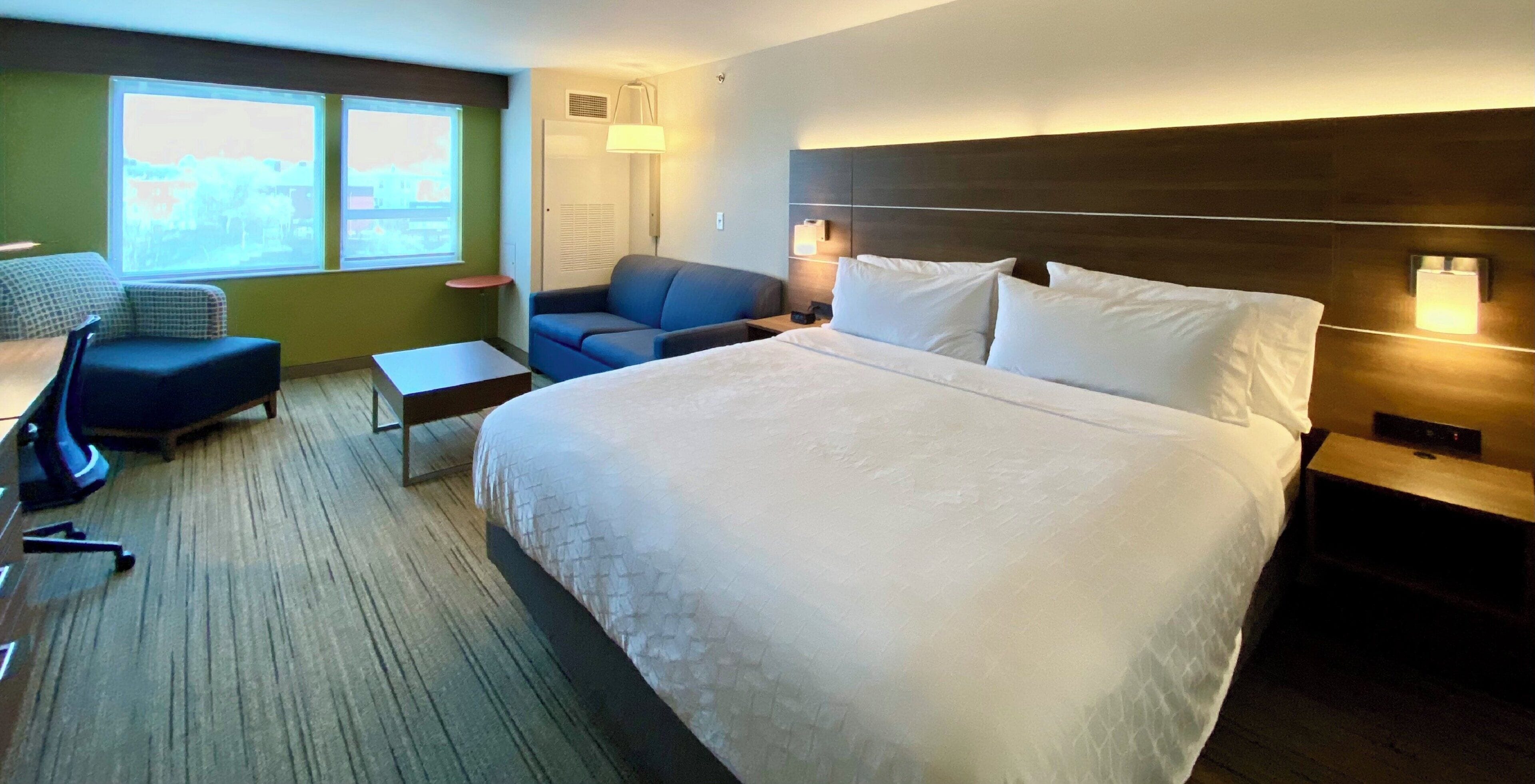 A hotel room with a large bed, a desk, a chair, a sofa, and a window with a view.