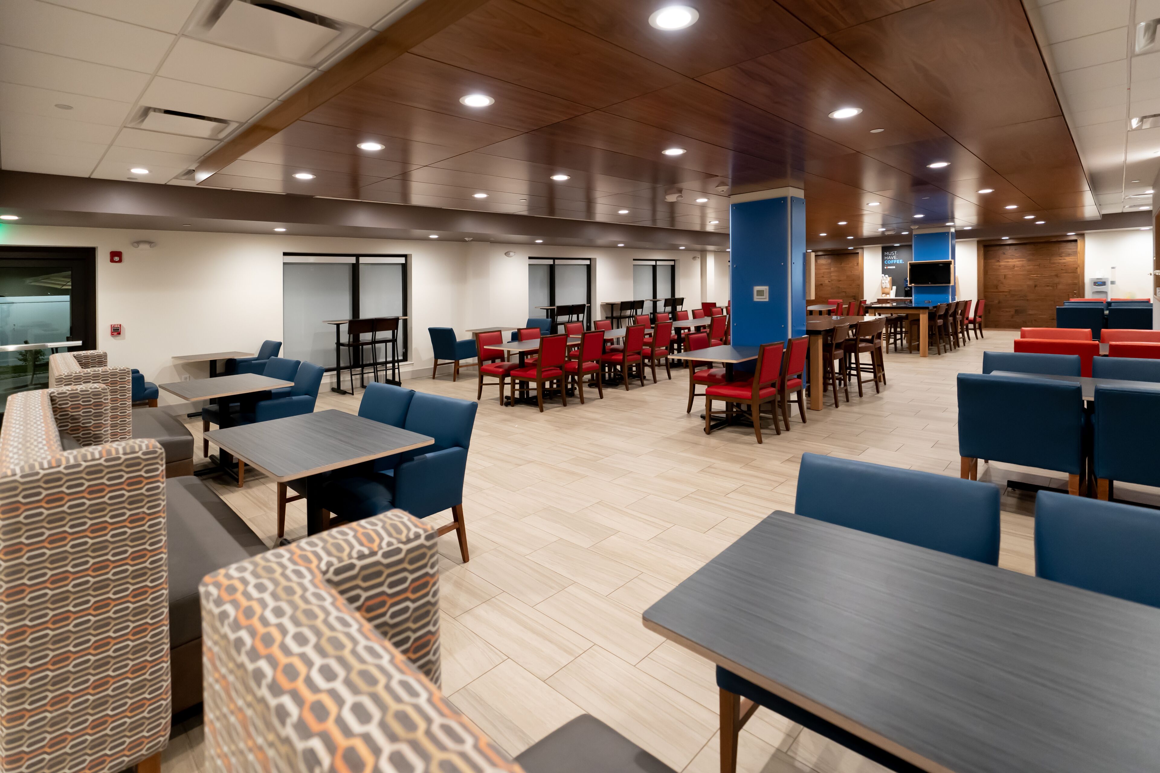 A spacious indoor dining area with multiple tables and chairs, wooden ceiling, and a modern design.