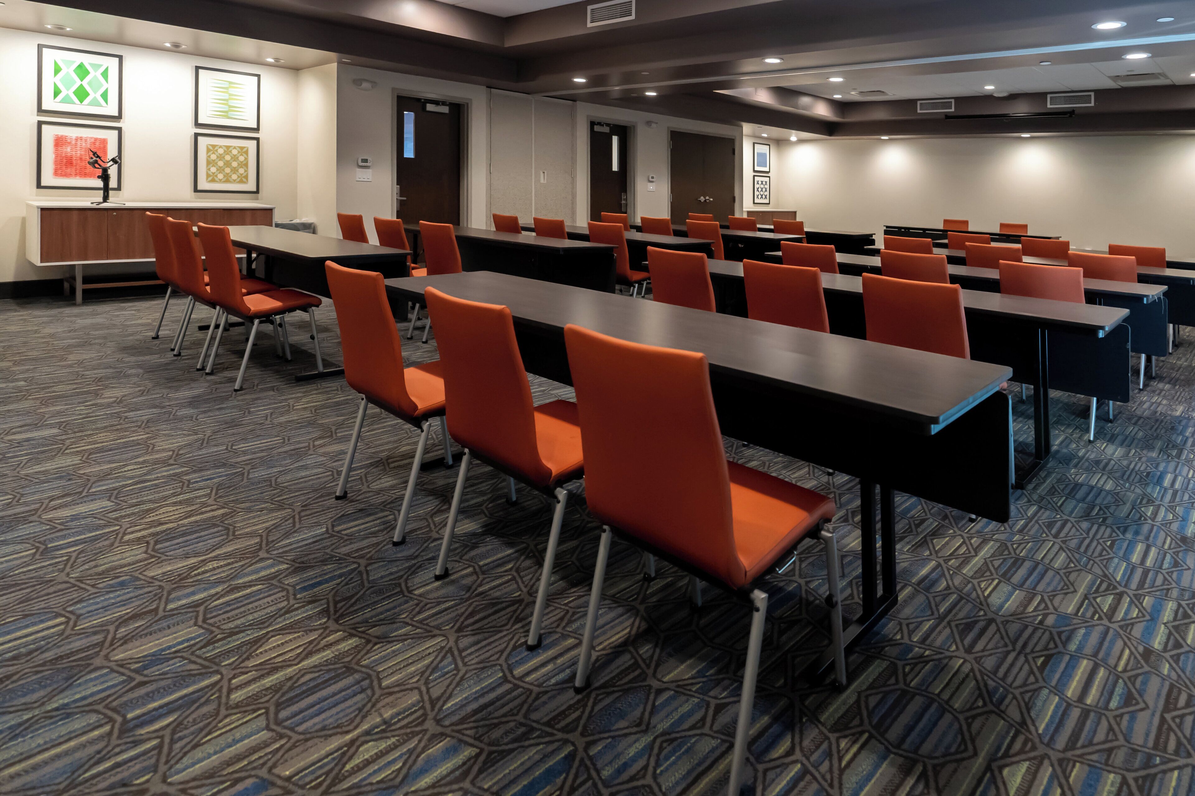 Une salle de conférence dotée de plusieurs tables et chaises, d’un tapis à motifs et d’œuvres d’art encadrées accrochées aux murs.