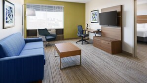 A hotel room with a blue sofa, a wooden desk, a flat-screen TV, a bed, and a window with a city view.