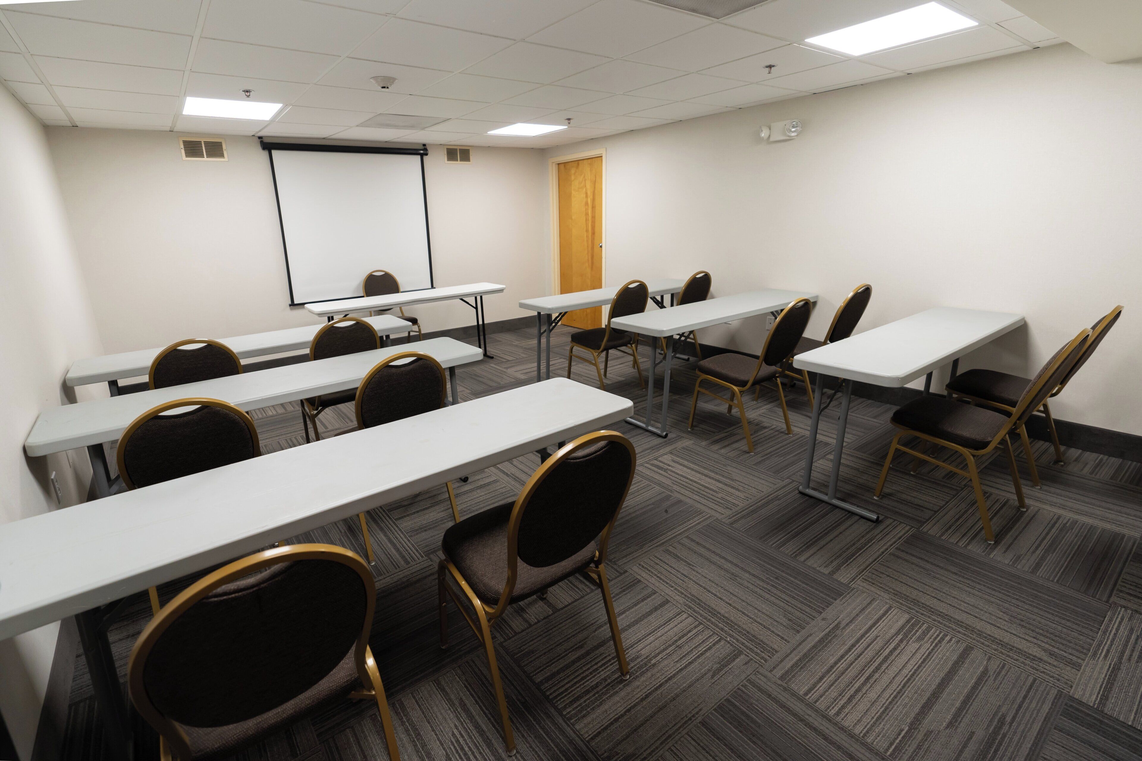 A conference room with multiple tables and chairs, a projector screen, and a whiteboard.