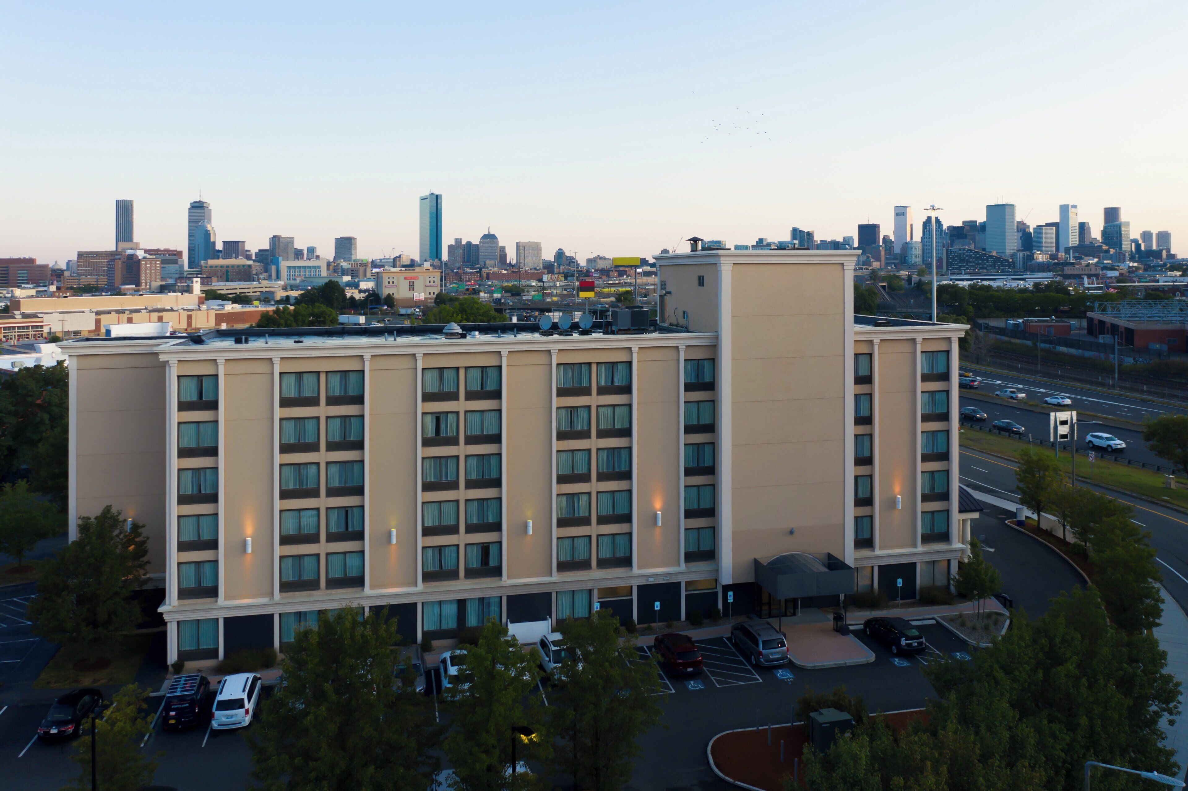 A multi-story hotel with a parking lot in front, surrounded by a city skyline.