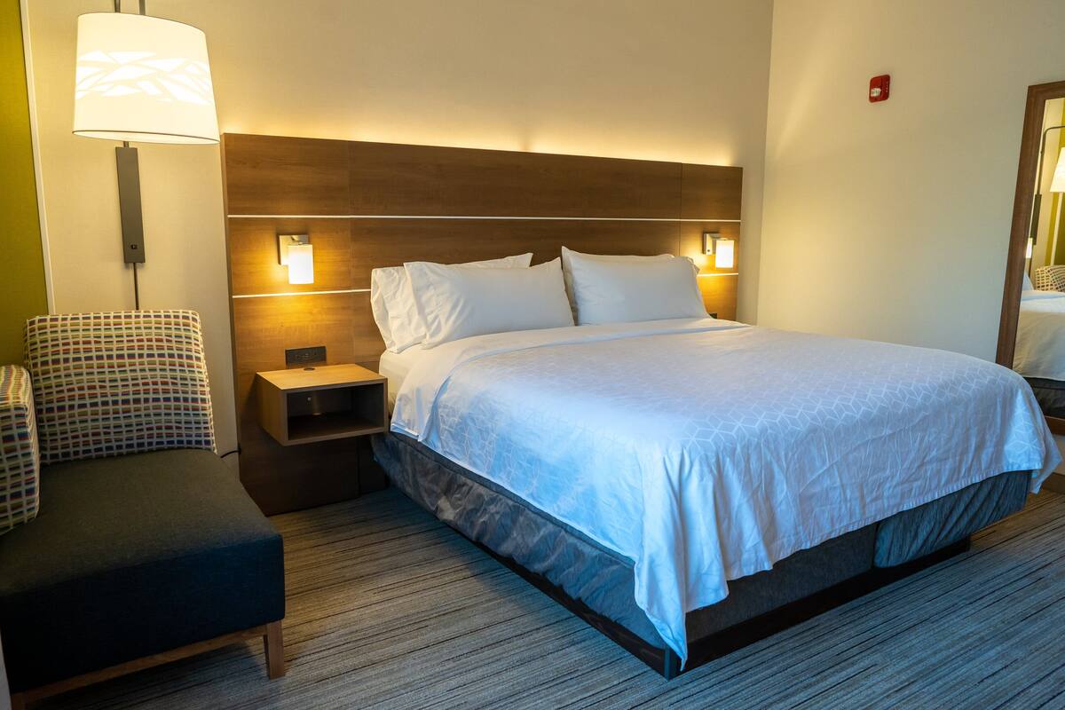 Een hotelkamer met een bed, nachtkastje, stoel en lamp.