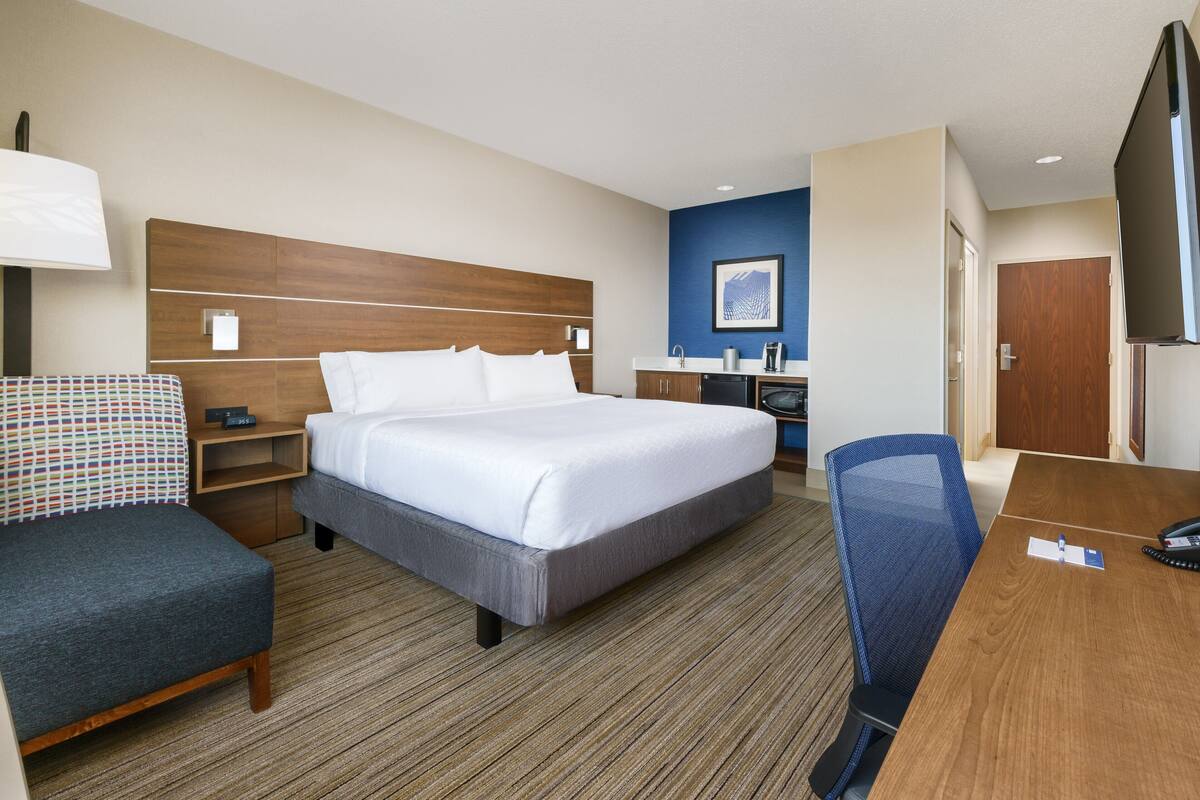 Een hotelkamer met een groot bed, een bureau, een stoel, een kleine kitchenette en een televisie.